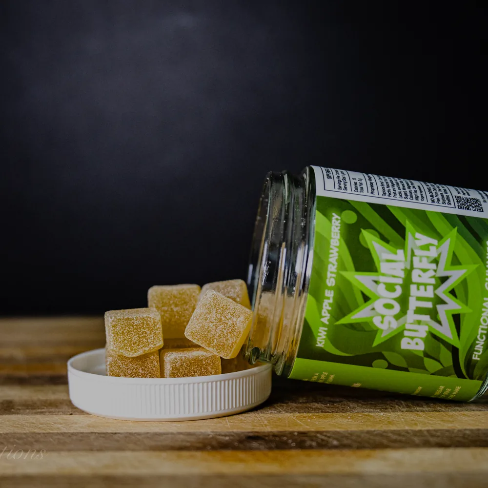 BAMM Social Butterfly glass jar with kiwi apple strawberry gummies on a dark studio backdrop.
